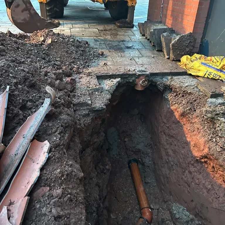 Picture of a digger digging up road to access collapsed drain pipe that needs repairs