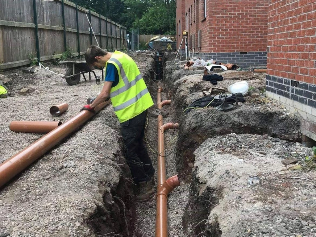 A picture of a man fitting drainage systems on a building site